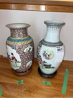 Two Asian porcelain vases side by side on a wooden surface, each on carved wood stands, sizes marked as 13.5 and 15 inches