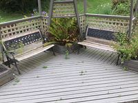 Wide view of both matching outdoor benches on a wooden deck with lattice fencing and greenery around.