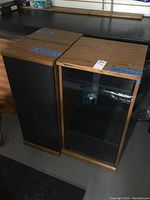 Pair of Technics speakers with wood finish and black fabric covers and Technics stereo cabinet with smoke glass door, all placed side by side on the floor.