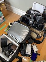 Overview of Nikon camera body with attached lens, extra lens, battery charger, battery, flash, light meter and carrying bags