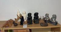 Wide angle showing all the items on a shelf including carved soapstone Foo Dogs, white carved figures, wooden mask, antler, bear figure, metal bicycle, and beaver tray.