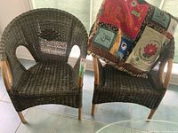 Two green wicker chairs with natural wood accents, along with a colorful decorative celebratory pillow draped on one chair.