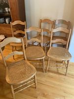 Set of six wooden chairs with caned seats and ladder backrest, showing natural wood finish and turned legs.