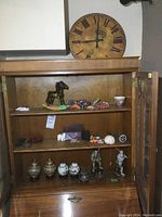 The open wooden cabinet containing assorted collectible items including the green rocking horse and various small urns and figurines.