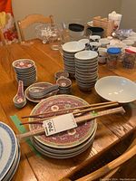 Overview of the set on dining table showing stacked bowls, plates, chopsticks, and spoons with Asian-themed patterns.