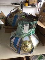 Photo of three glass hanging lights with brass chains on a shelf, two lights have stained glass and floral etched designs, one is a ceiling hugger type.