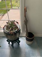Photo of large ceramic jardinier planter with Christmas cactus and dark wooden stand, next to a #2 crock holding an umbrella.