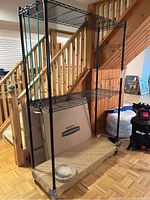 Front and side views of black metal wire shelving unit with four shelves and caster wheels, beige mat on bottom shelf, six green bungee cords attached vertically for added support.