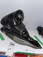 Front three-quarter view of black soapstone carving showing kneeling man and seal on flat base
