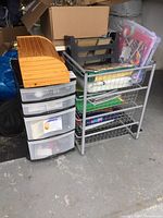 Photo of plastic storage organizer with drawers filled with light bulbs, metal shelf with wire drawers holding file folders and books, and wooden bread box on top.