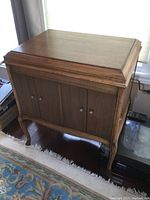 Wooden antique Victrola record player cabinet showing front closed with panel doors and curved legs.