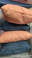 Four outdoor pillows stacked in a bin, two orange striped and two dark blue striped pillows visible.
