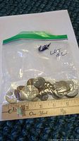 Plastic resealable bag containing mixed assorted coins of various sizes and metals, measured on a ruler.