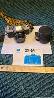 Minolta XG-M camera with attached lens next to the camera case and original instruction manual on carpet