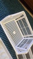 Photo showing white plastic basket, rectangular with perforated sides and base