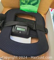 Photo showing black Ortho Fix Spinal-Stim back brace with digital stimulation device and adjustable straps inside packaging box.