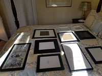 Photo of 10 black photo frames laid out on a bed with patterned bedding, showing various sizes and some with matt boards