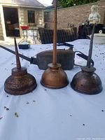 Three antique metal oil cans arranged side by side on a white surface, showing varying degrees of wear and rust.