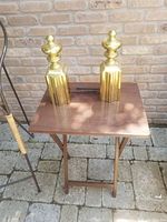 Pair of brass firedogs standing on a small wood table, showing the full view with the fluted base and urn finials.