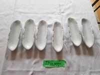 Six white ceramic corn on the cob holders laid out on a table, showing their elongated shape and textured surface mimicking corn.