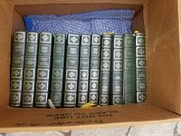 11 hardcover Charles Dickens books with green covers and gold embossed titles in a cardboard box.