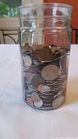 Glass jar filled with assorted foreign coins of various sizes and colors