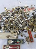 Wide view of a mixed heap of collector spoons showing many different decorative handles and some spoons still in original packaging.