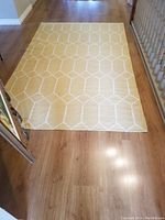 Photo of a yellow wool kilim rug with white geometric diamond pattern displayed on a wood floor, full view showing entire rug.