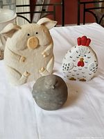 Front view of pig, chicken, and hollow dove on a white surface, showing their size and details