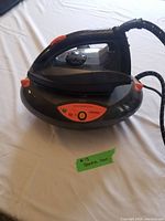 Full view of the black and gray steam iron placed on its base, showing its ergonomic handle and fabric-covered steam cord.