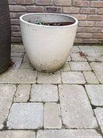 Front-side view of the large beige ceramic planter placed on a stone tile patio, showing some dirt marks near the base.