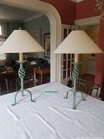 Pair of green metal table lamps with beige shades on a white tablecloth in a living room setting, showing overall appearance and dimensions.