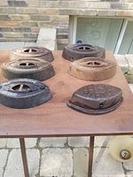 Six vintage sad irons arranged on a wooden table outdoors, showing front and side views of each iron, highlighting rust and wear.