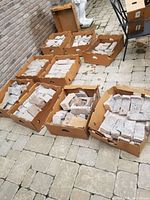 Multiple cardboard boxes containing numerous light gray stone veneer pieces laid out on a stone paver surface.
