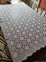 Full view of white crocheted tablecloth spread out on table showing intricate crochet pattern and scalloped edges