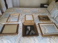 Six gold picture frames arranged on a bedspread, one containing a framed black and white portrait.