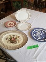 Five various small china plates and platters arranged on a white cloth, showcasing different decorative patterns including floral and blue willow designs.