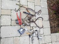 Full view of assorted hand tools on stone surface including meat grinders, handheld grater, sickle, and clamps.