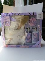 Front view of the boxed bath and beauty set showing all included items: bathrobe, body scrubber, and three lavender bath products in a ribboned box.