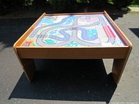 Front and side view of wooden children’s train table with colorful reversible top showing train track design