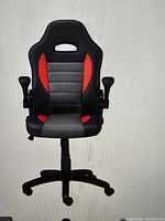 Gaming chair front view showing black and red upholstery, contoured back, and armrests.