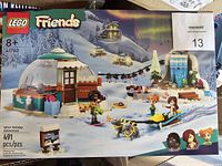 Box front image showing the full Lego Friends Igloo Holiday Adventure set, including igloo, sled dogs, mini-figures, and winter accessories under northern lights background.