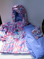 Full view of girls' Mountain Warehouse winter snow suit on white background showing jacket with hood and snow pants folded over