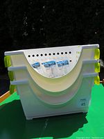 Three stacked white plastic organizer baskets with green handles and holes on sides, placed outdoors on a wooden surface.