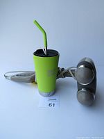 Photo showing a green insulated cup with a black lid and green straw alongside a portable plug-in massager with two silver rounded heads, white handle with inline controls and attached power cord.