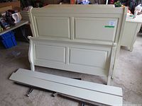 Full view of disassembled queen size off white sleigh bed frame parts arranged on the floor including headboard, footboard, and side rails.
