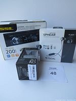 Photo showing the boxed Sound Storm Labs ML46DB car receiver, Focal Spear S earphones box, and ZOKO wireless speaker box with lot tag 48