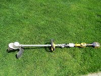 Long view of the full weed wacker showing its full length, yellow and black color, the handle, and protective guard for cutting head.