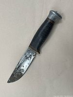 Photo of the full knife showing the leather stacked handle with metal pommel and steel blade with wear spots.