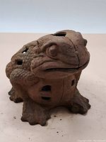 Front angled view of the cast iron frog lawn ornament showing its textured body and facial features with rust and wear.